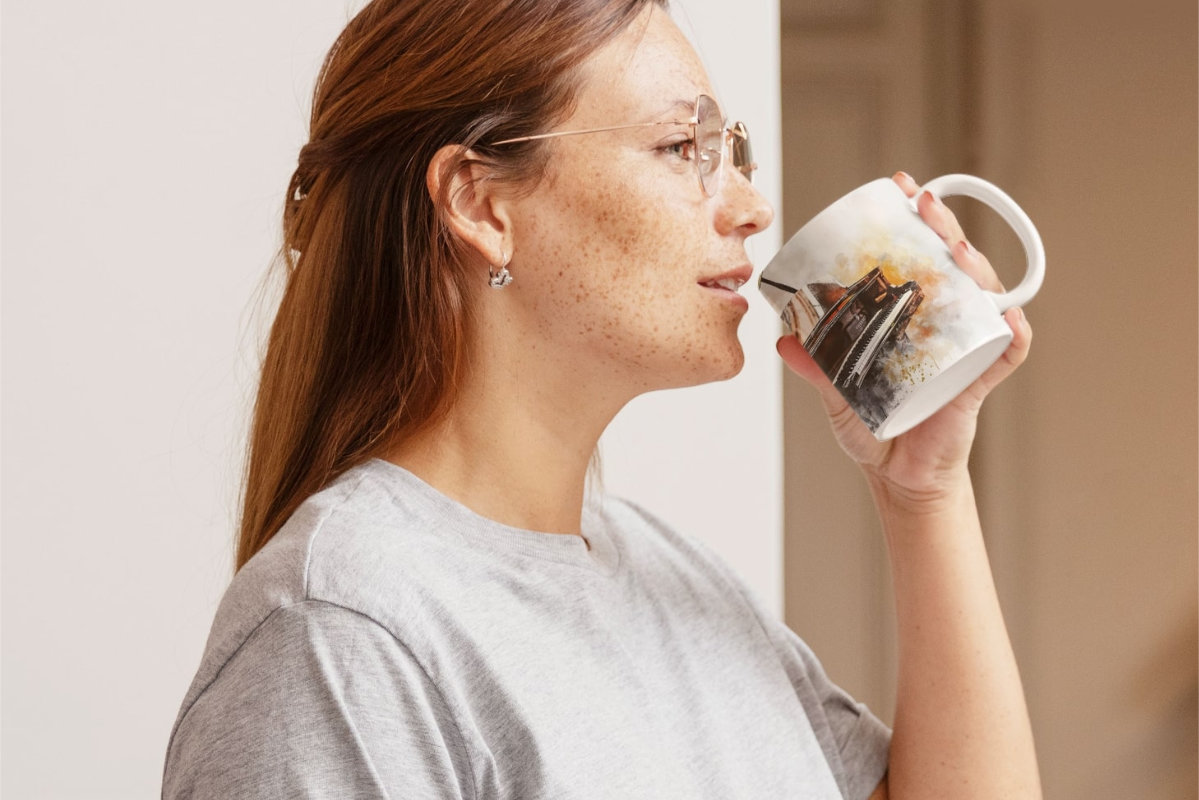 Frau mit Brille hält eine Kaffeetasse mit einem Piano motiv in der Hand, während sie daran nippt.