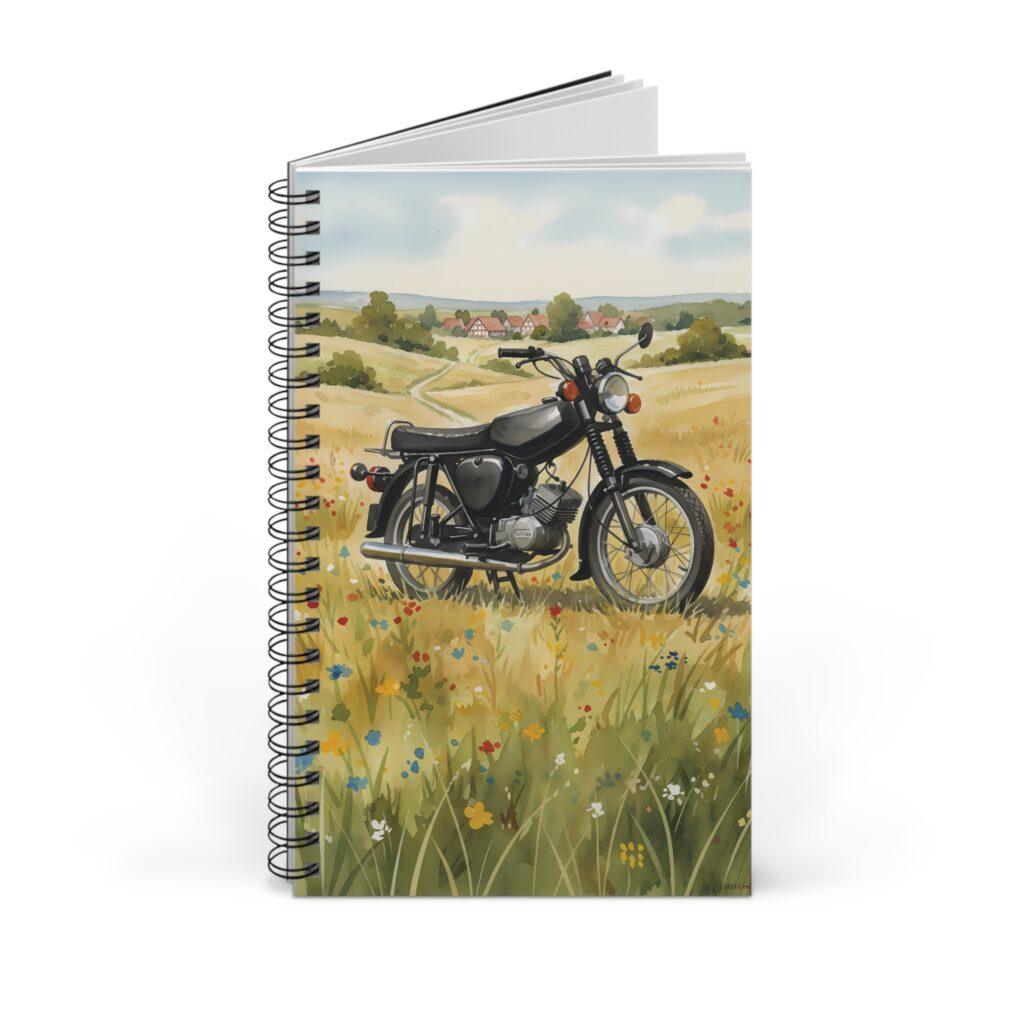 Ein schwarzes Simson S51 auf einer bl&uuml;henden Sommerwiese vor sanften H&uuml;geln, als Aquarellmotiv auf einem Ringbuch-Notizbuch.